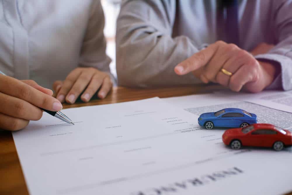 Personne signant un contrat d'achat de voiture, avec un document de divorce en arrière-plan.