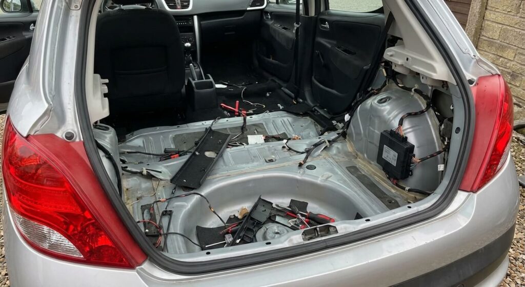 Où se trouve le boîtier de radar de recul sur Peugeot 207 ? 9 Intérieur du coffre d'une Peugeot 207 dégarni, montrant l'emplacement du boîtier de radar de recul sur le passage de roue droit.