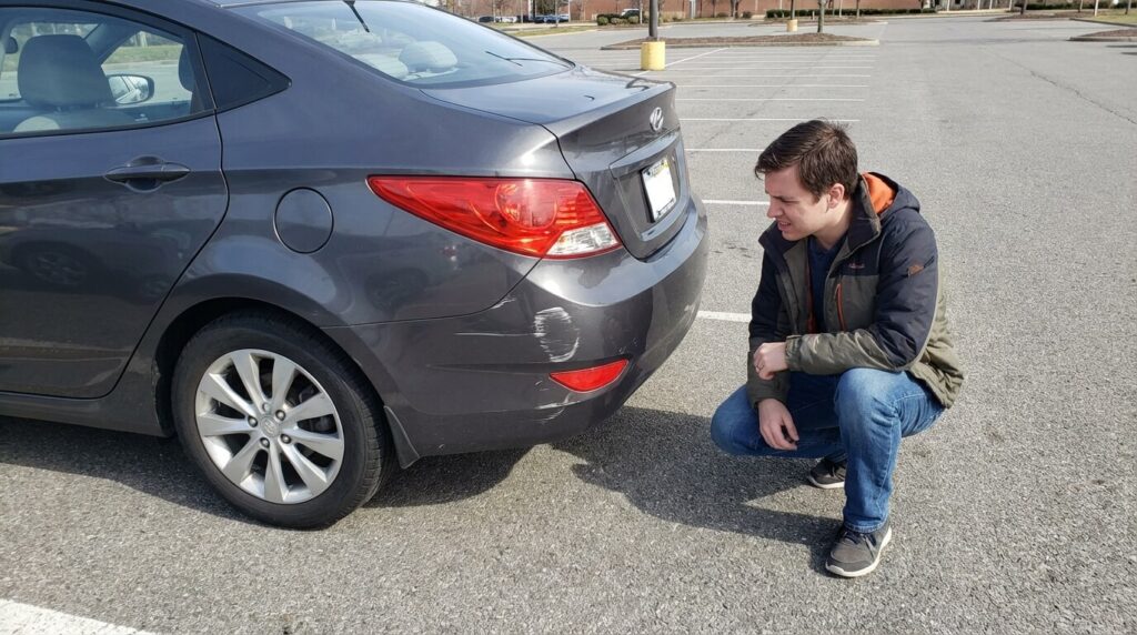 Pare-choc de voiture rayé sur un parking avec le conducteur constatant les dégâts sans tiers identifié