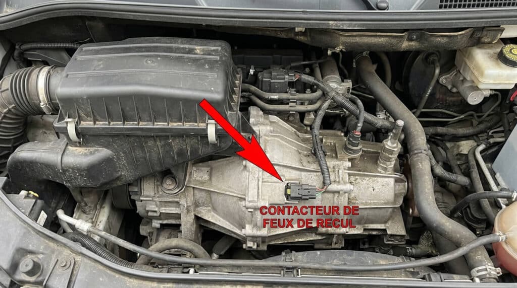 Vue du dessus de la boîte de vitesse d'un Fiat Ducato 2.3 Multijet, flèche indiquant le contacteur de feux de recul sous le filtre à air