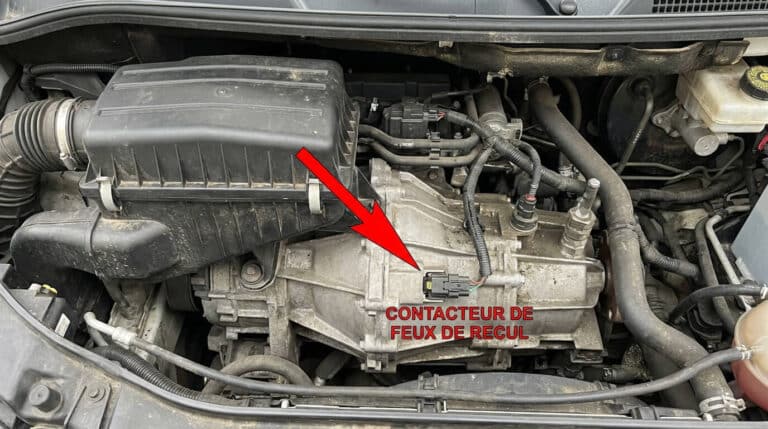 Vue du dessus de la boîte de vitesse d'un Fiat Ducato 2.3 Multijet, flèche indiquant le contacteur de feux de recul sous le filtre à air