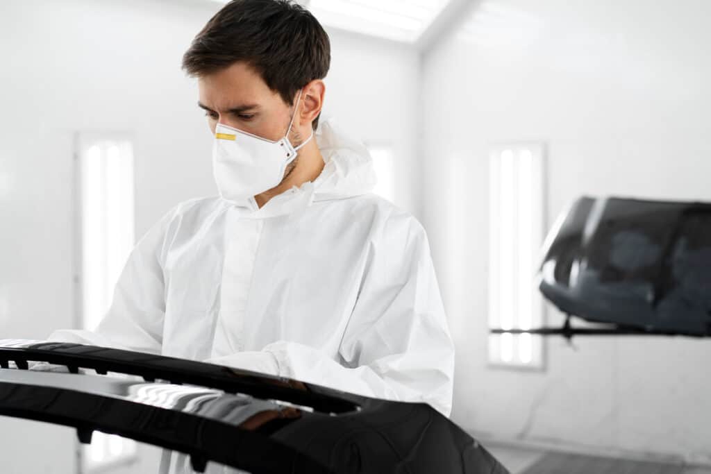 Application d'une couche de peinture métallisée sur une aile de véhicule dans une cabine de peinture professionnelle ventilée.
