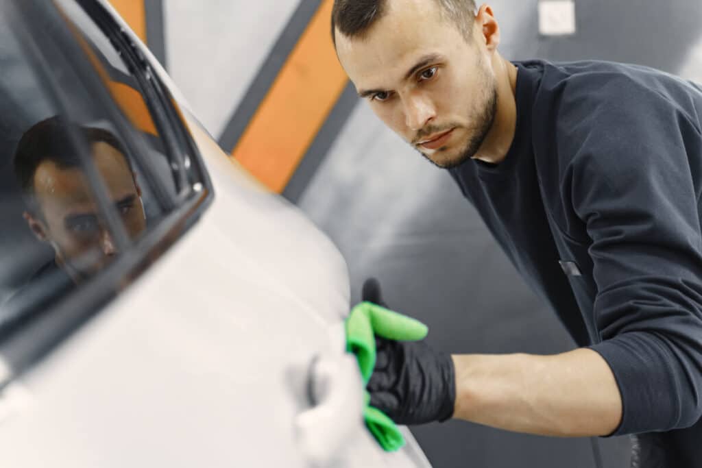 Un carrossier professionnel utilisant des outils de précision pour redresser une bosse sur la portière d'une voiture.
