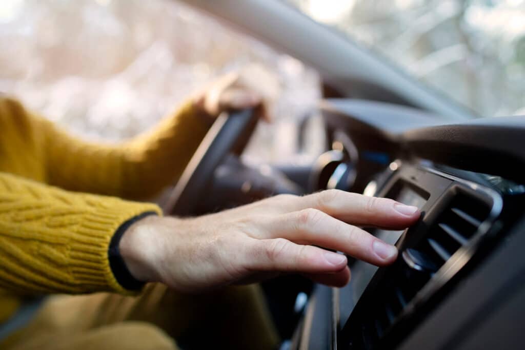 Gros plan sur la main d'un conducteur ajustant la grille d'aération ou les commandes de climatisation sur le tableau de bord de sa voiture.