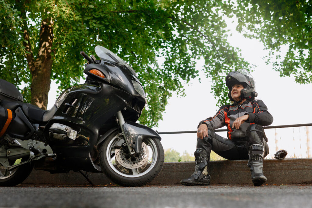 Panne ou casse mécanique : l'assurance moto couvre-t-elle ? 2 Un motard à côté de sa moto à l'arrêt sur le bas-côté, attendant une dépanneuse.