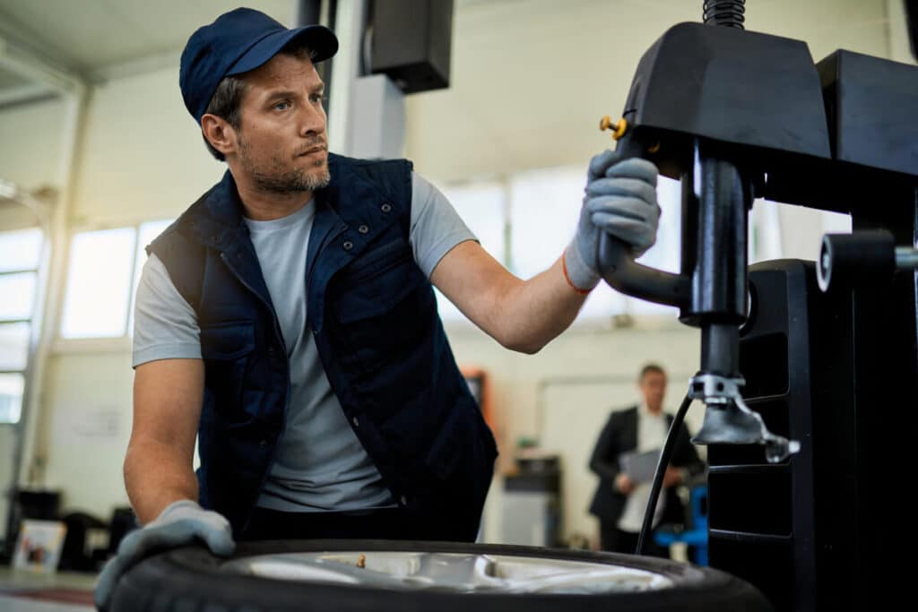 Quand et comment changer les pneus de sa voiture ? 3 Un technicien de centre auto utilisant une machine démonte-pneu professionnelle pour installer un pneu neuf sur une jante alu.