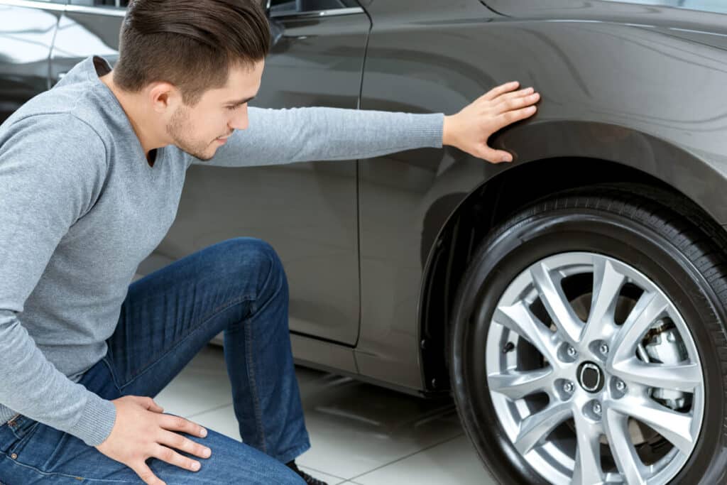 Quand et comment changer les pneus de sa voiture ? 2 Un automobiliste inspectant le témoin d'usure en caoutchouc situé au fond des sculptures d'un pneu de voiture.