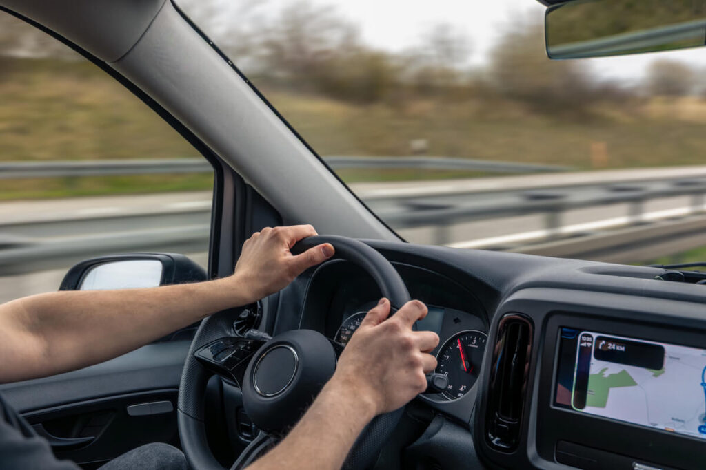 Les mains d'un conducteur maintenant un volant légèrement incliné pour garder sa voiture droite sur la route.