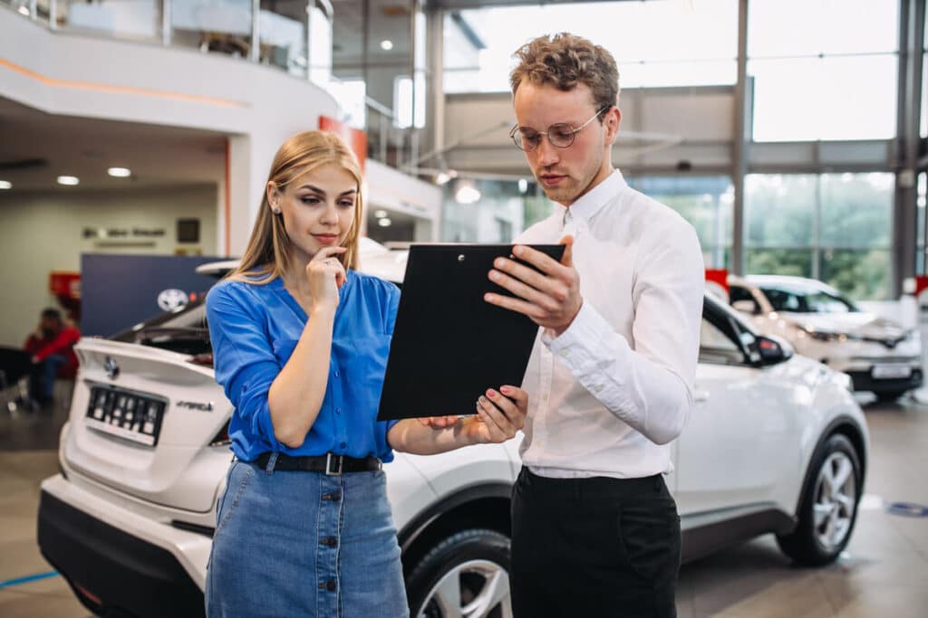 Vendeur automobile renseignant un client dans une concession pour l'achat d'un véhicule.