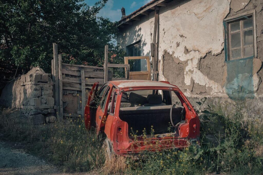 Une voiture épave abandonnée garée devant l'entrée d'une maison individuelle.