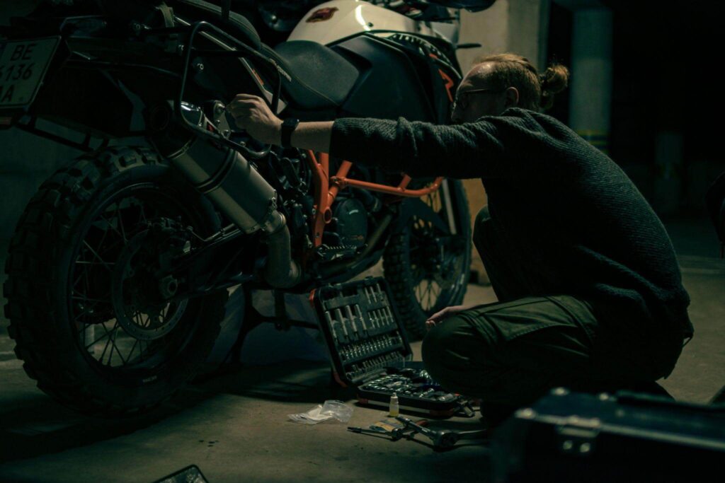 Mécanicien moto réparant le bloc moteur d'une moto posée sur un pont élévateur en atelier.