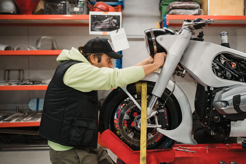 Apprenti mécanicien moto suivant les conseils d'un tuteur d'atelier pour le réglage d'une fourche.