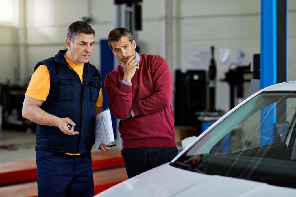 Expert en assurance automobile chiffrant les dommages sur une voiture accidentée dans un garage.