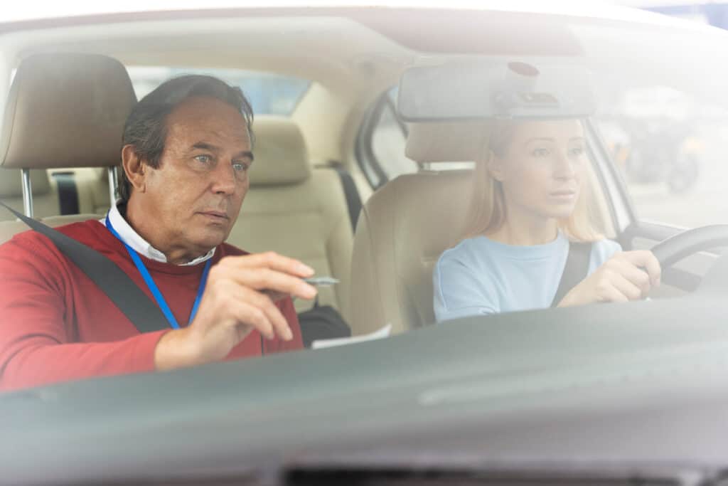 Permis raté 15 fois : que faire pour enfin l’obtenir ? 2 Inspecteur du permis de conduire tenant le bordereau d'évaluation officiel aux côtés du candidat.