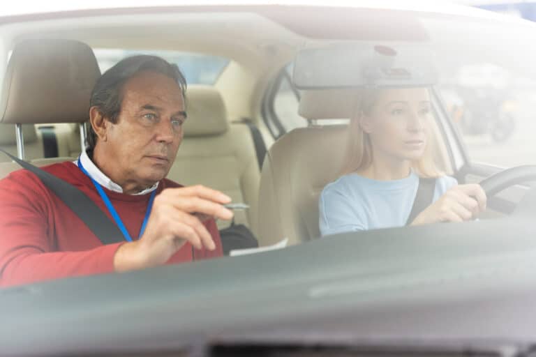 Inspecteur du permis de conduire tenant le bordereau d'évaluation officiel aux côtés du candidat.